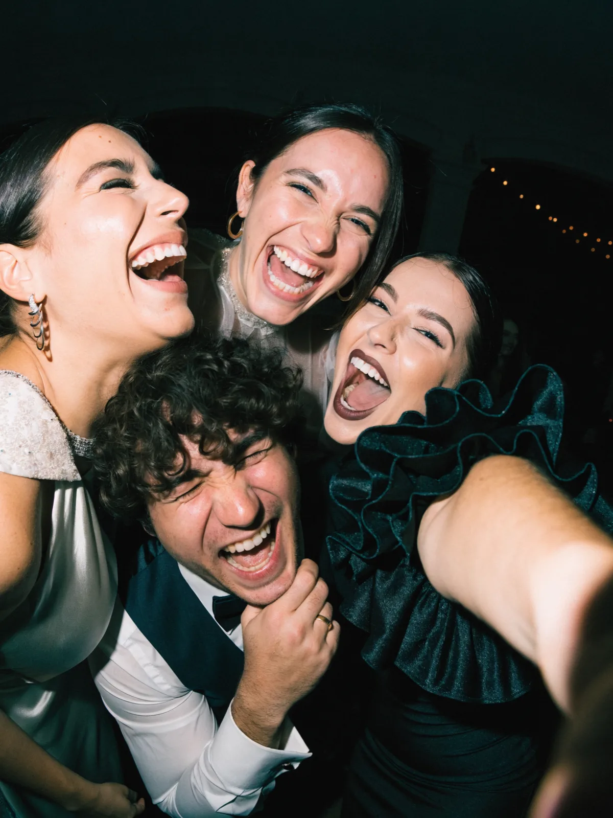 Four wedding guests squeezed into a flash-lit selfie on the dance floor, all laughing