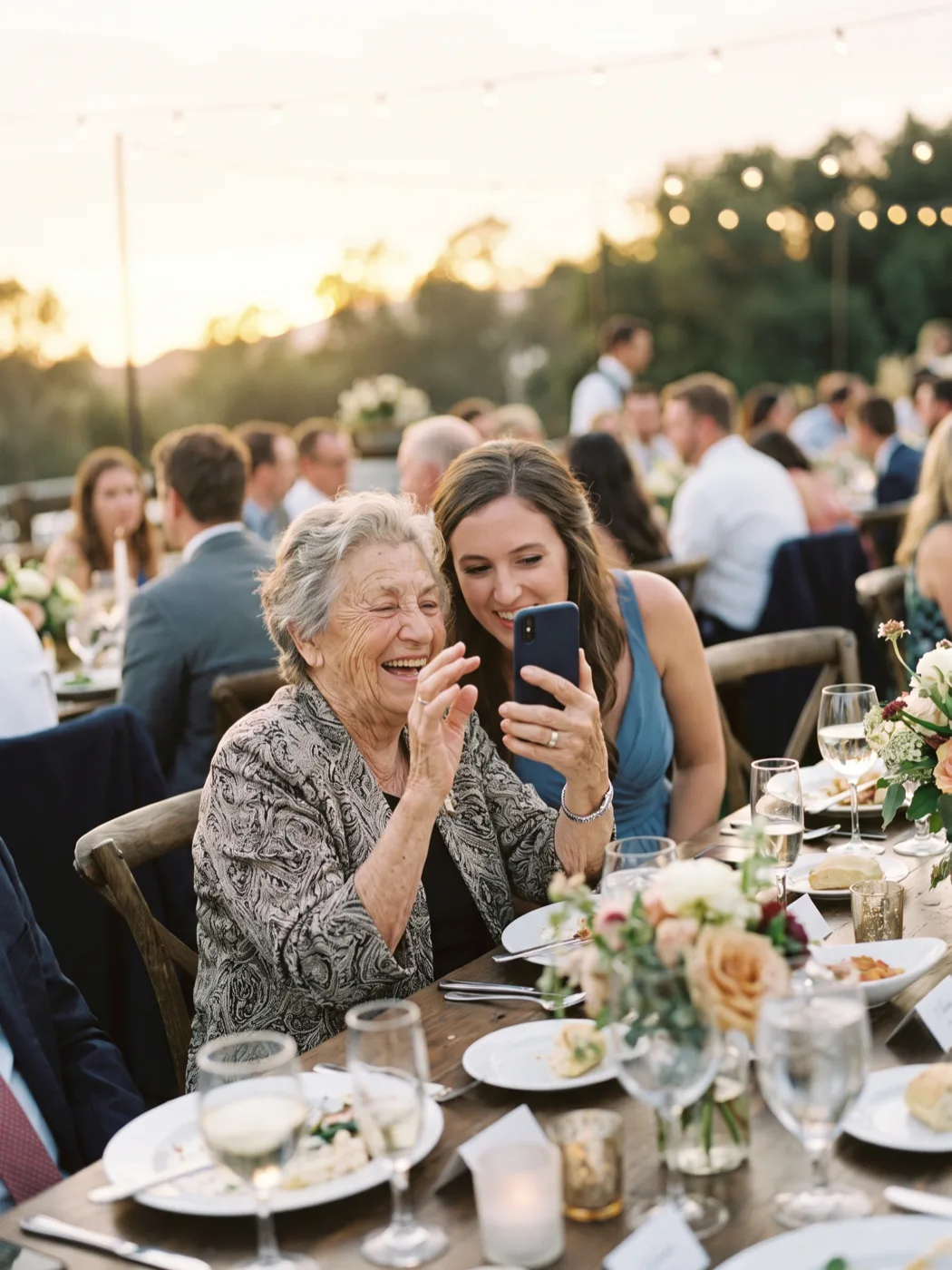 A grandmother laughing while a younger guest records a video message of her